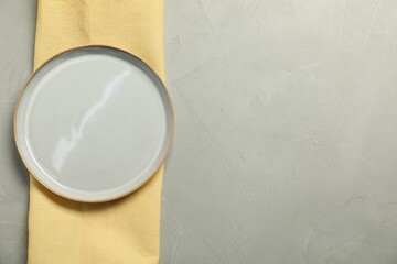 Yellow napkin and empty plate on grey table, top view. Space for text
