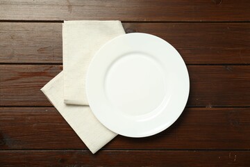 Light napkin and empty plate on wooden table, top view