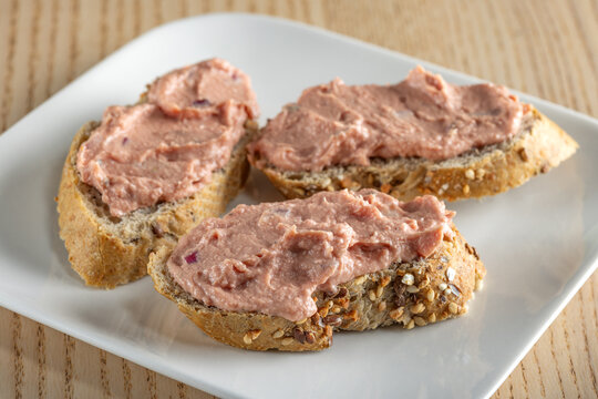 Three slices of bread spread with a pink, smooth, and spreadable p&acirc;t&eacute; made with red onion and butter.
