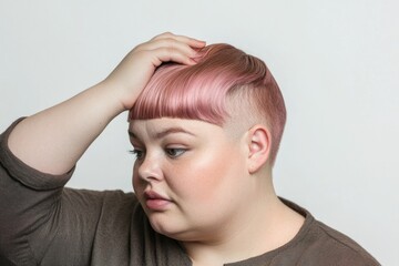 Fototapeta premium A girl with pastel pink hair styled in a unique way touches her head with a contemplative expression, highlighting modern hairstyles and youthful beauty.