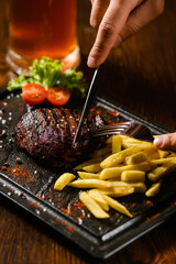 Juicy steak with fries and beer on dark table.