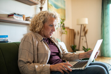 Shocked middle aged woman using laptop at home