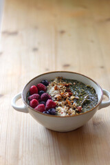 Beige bowl with green smoothie, frozen berries and homemade granola, served on the table. Selective focus.