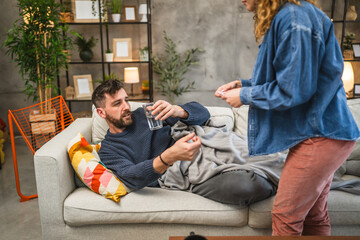 wife give medicine and water to husband while he lying down on sofa