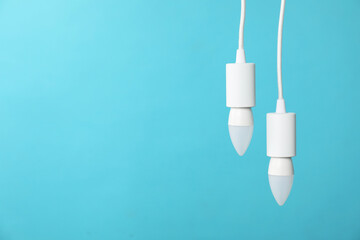 Light bulbs hanging on cords against blue background, space for text