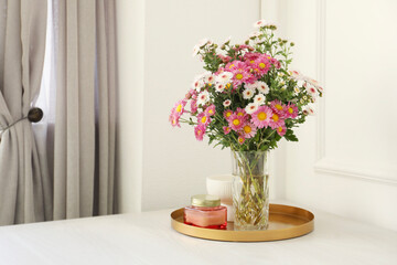 Beautiful flowers in vase and candles on white wooden table at home