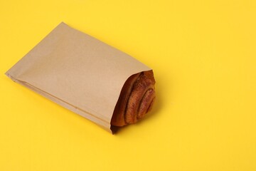 Paper bag with freshly baked bun on yellow background. Space for text