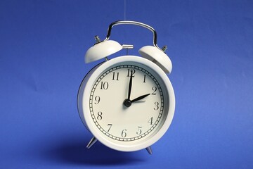 White alarm clock in air on blue background