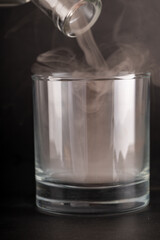 A close-up shot of a clear glass tumbler being filled with thick, white vapor. The vapor pours from...