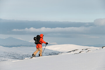 Close-up of a skier in an orange jacket and full gear skiing across the snow