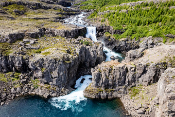 Scenic aerial view of a rocky Nykurhylsfoss (Sveinsstekksfoss) waterfall surrounded by lush green landscape near Fossardalur Campsite in Iceland