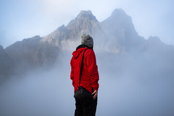 Solitary hiker in red jacket standing amid foggy Vestrahorn mountainous landscape breathtaking...
