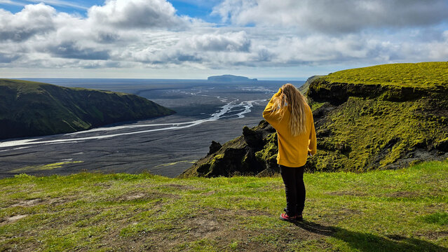 Woman in yellow sweater admiring scenic landscape glacial basin with river and green mountains under cloudy sky very close to Thakgil (Pakgil) campsite near Vik in Iceland