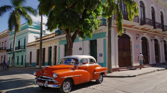 Picturesque Havana streetscape showcasing a classic orange vintage car parked alongside colorful colonial buildings, with pedestrians strolling by, capturing the timeless charm of Cuba