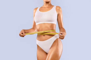 Perfect Body Concept. Cropped close up view of slim woman in white top and panties measuring her...