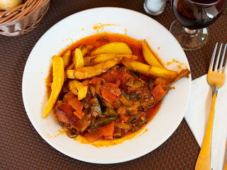 French fries and rabbit with samhain sauce are served with glass of red wine. vegetable dish stew from chef of restaurant is prepared according to recipe of Catalan cuisine.