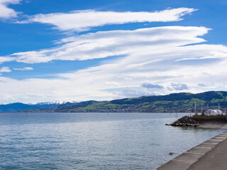 Arbon, Switzerland - March 29th 2024: At the bank of Lake Constance in front of the Alps with typical Foehn clouds