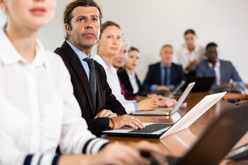 Businessman using laptop during conference in meeting room. Man sitting at desk with colleaugues.