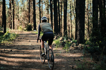 Fototapeta premium Cyclist rides gravel bike through sun-dappled forest path. Peaceful, adventurous scene perfect for travel, sports, and nature themes.