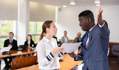 Obraz premium Irate adamant middle aged african male director dismissing frustrated and upset young white female subordinate employee for incompetence telling her to get out of office pointing to the door at