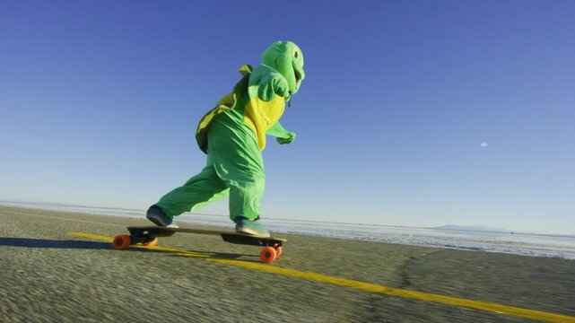 Epic yet silly shot of person in frog costume longboarding down desert road at sunset - low, steady cam
