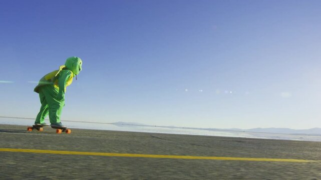 Longboarder in funny frog costume riding down road at salt flats in Utah - wide, steady cam shot