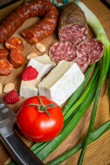 Bright sliced sausages and cheeses with vegetables and herbs lie on a board