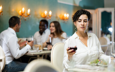Single woman eating and drinking at the restaurant with a multiracial group of people on the background