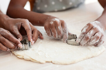 Closeup of black family mother and daughter hands making diverse figures with cookie cutters, happy african american mom and kid baking together at home, using biscuit figurines, baking concept