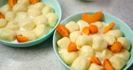 Close-up of hands decorating dumplings with sour cream and apricot on blue plate, against granite background. Ideal for food enthusiasts seeking culinary inspiration.