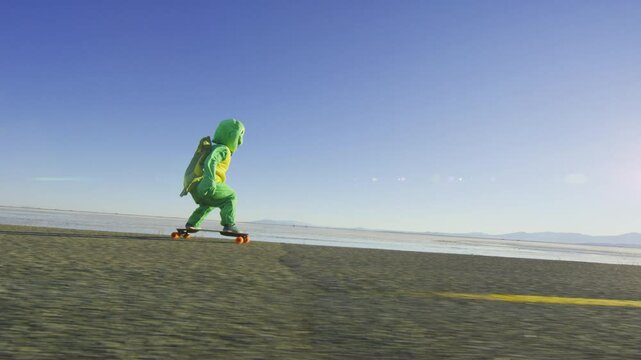 Person in turtle costume speeding down desert road on longboard - wide, steady cam shot
