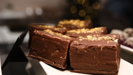 Large delicious bird's milk dessert chocolate coating yellow sprinkles white plate displayed counter indulgent sweet treat perfect for dessert lovers rich creamy texture elegant presentation