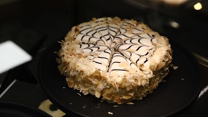 Beautiful black white hazelnut esterhazy cake topped almond slices on black plate on countertop elegant gourmet dessert rich layers flavor luxury pastry sweet indulgence sophisticated confection