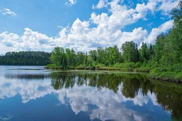 beautiful summer landscape with forest and blue sky with white clouds reflecting in water