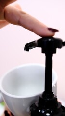 Barista adds red cherry syrup to a white coffee cup using a dispenser at a coffee shop creating a delicious flavored drink with vibrant color perfect for coffee lovers seeking refreshing beverages