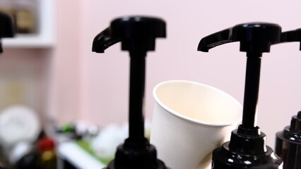 Barista adds red cherry syrup to a white paper coffee cup using a dispenser at coffee shop creating delicious flavored drink with vibrant color perfect for coffee lovers seeking refreshing beverages