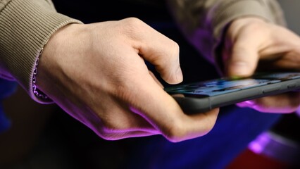 Young man playing mobile game with fast finger movements and colorful pulsating hand lights, dynamic gameplay, close up phone screen, digital entertainment, gaming action, energetic gaming session.