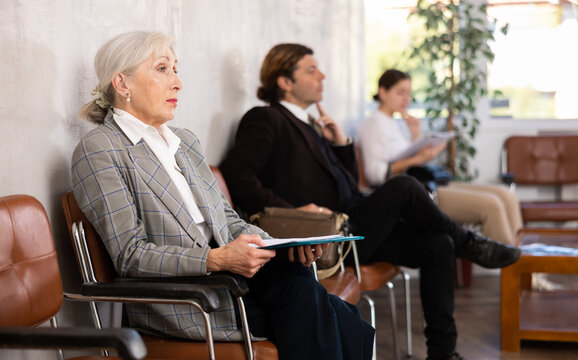 Unemployed senior woman is waiting for job interview in waiting room. Anxious female applicant with resume is waiting for invitation to recruiter s office