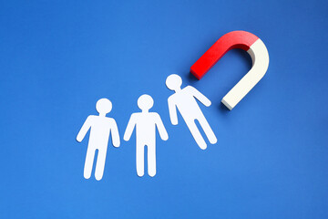 Magnet attracting paper human figures on blue background, flat lay