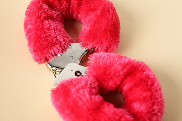 Pink fluffy handcuffs on pale yellow background, top view. Sex toy