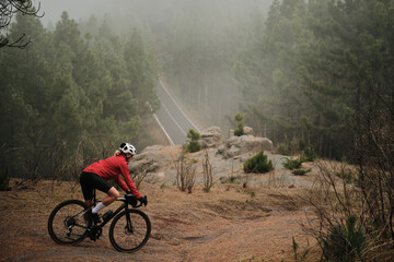 A cyclist in red jacket rides gravel bike on a foggy mountain road. Epic landscape photography...