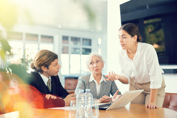 Adult man, elderly woman and young woman in business clothes having meeting in office