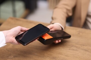Woman paying with smartphone via terminal at wooden counter indoors, closeup