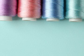 Different spools of sewing threads on light blue background, flat lay. Space for text