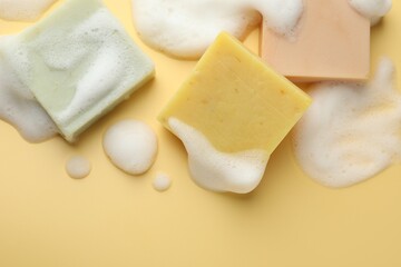 Soap bars with foam on yellow background, flat lay