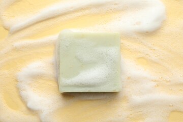 Soap bar with foam on yellow background, top view