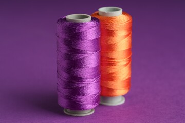 Different spools of sewing threads on violet background, closeup