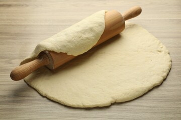Fresh dough and rolling pin on wooden table, closeup