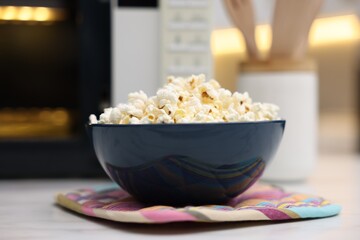 Tasty popcorn in bowl near microwave oven on light table indoors, closeup