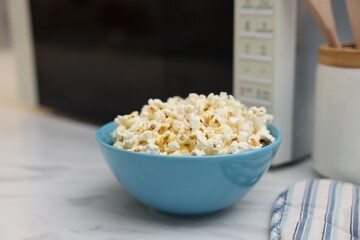 Tasty popcorn in bowl near microwave oven on white marble table, closeup. Space for text